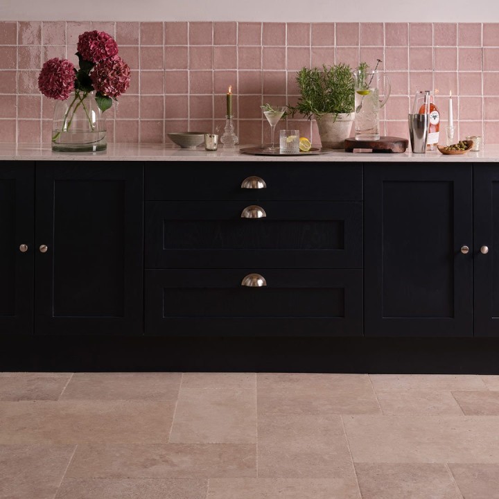 Handmade rose pink square tiles behind navy kitchen cabinets with kitchen accessories on top and a french limestone floor.