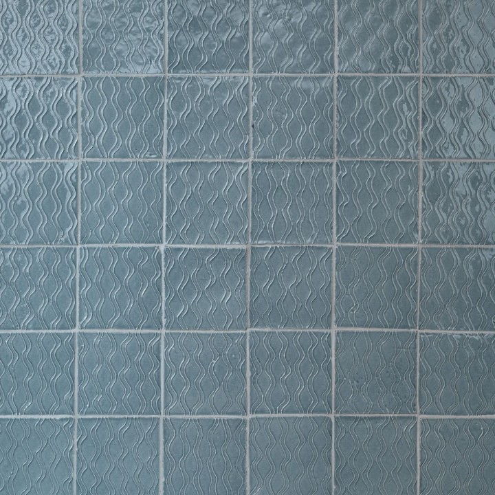 Wall of artisan rustic handmade subtle blue square tiles with a hand piped pattern with beige grout