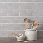 Wall of skinny pale grey tiles with white grout behind a utensil pot and wood worktop