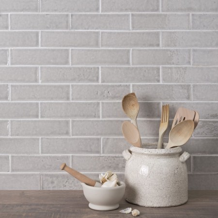 Wall of skinny pale grey tiles with white grout behind a utensil pot and wood worktop