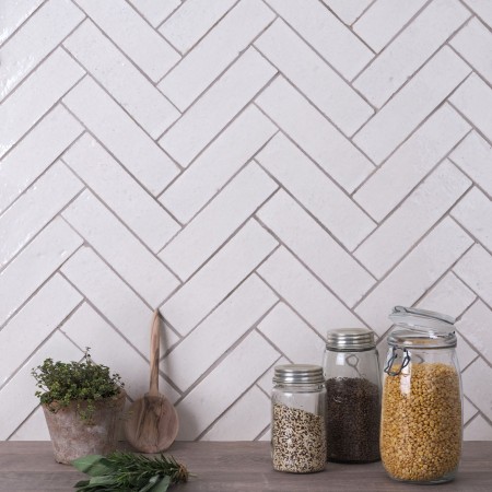 Wall of skinny warm white tiles with limestone grout behind kitchen accessories