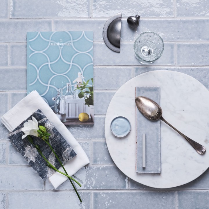 Flatlay of skinny blue tiles with silver grey grout in the background and kitchen hardware and accessories on top.