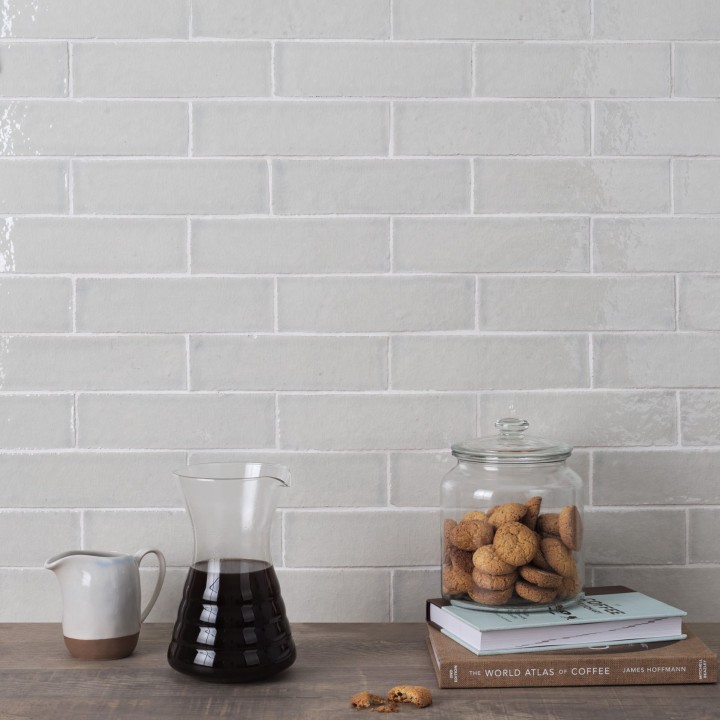 Wall of skinny soft green tiles with white grout behind a coffee pot and biscuit barrel