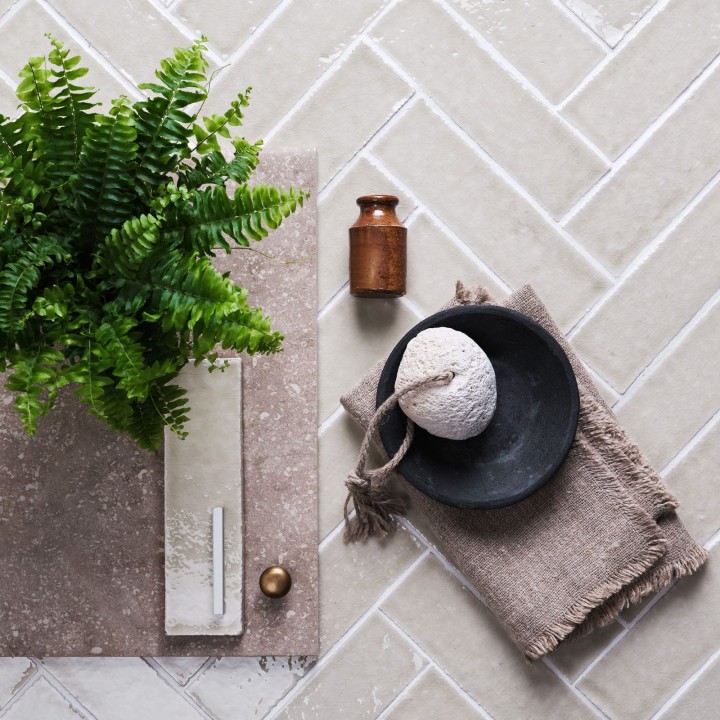 Flatlay of skinny beige tiles with white grout in the background and bathroom accessories and house plant on top.