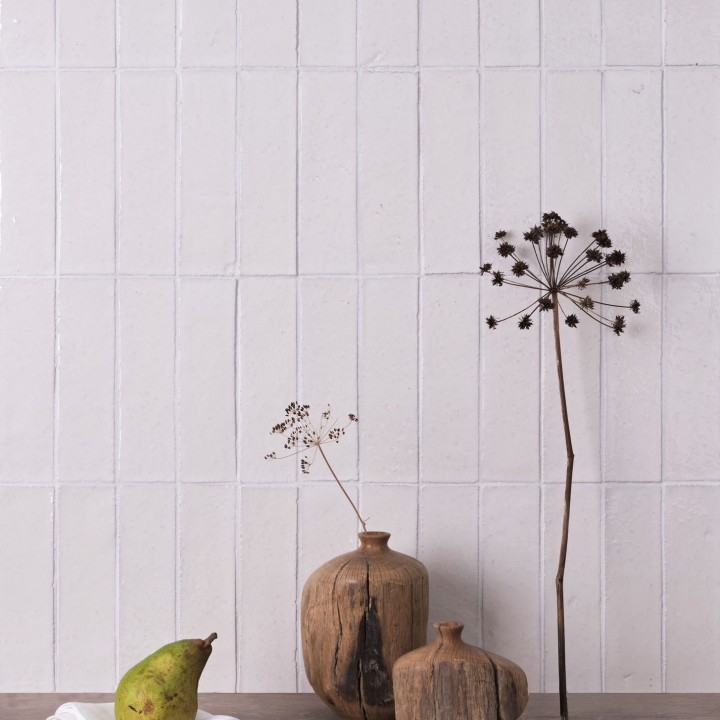 Wall of skinny chalk white tiles with white grout behind wood vessels with sedums