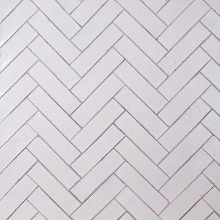 Wall of skinny warm white tiles with limestone grout laid in herringbone pattern