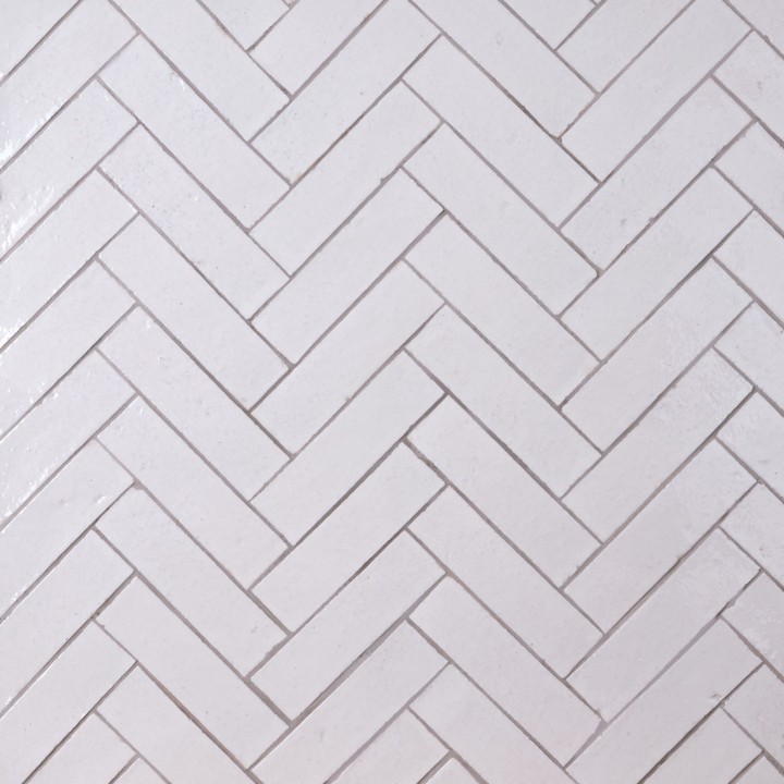 Wall of skinny warm white tiles with limestone grout laid in herringbone pattern