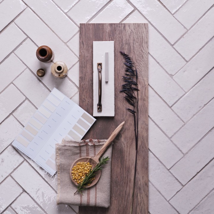 Flatlay of skinny warm white tiles with limestone grout in the background and kitchen hardware and accessories on top.