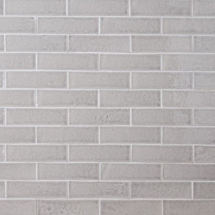 Wall of skinny pale grey tiles with white grout laid in a classic brick bond pattern