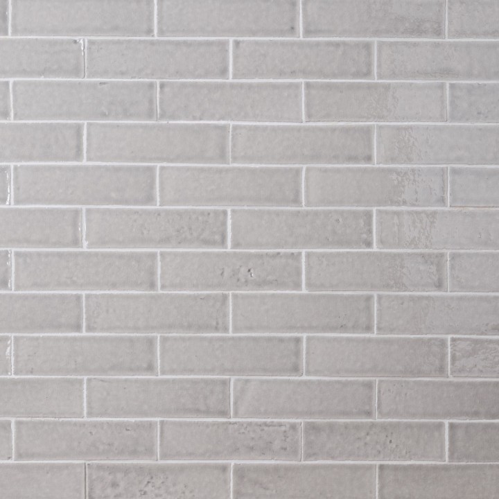 Wall of skinny pale grey tiles with white grout laid in a classic brick bond pattern