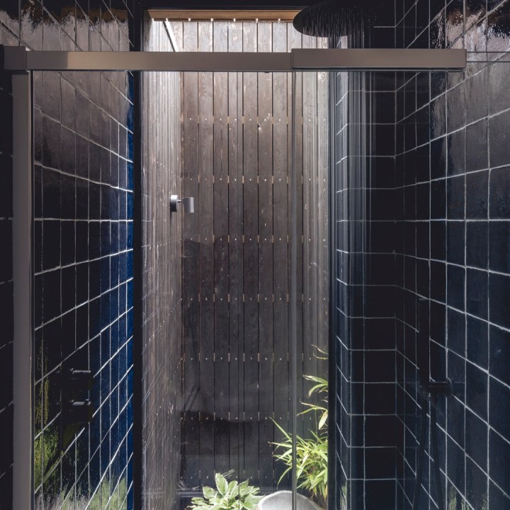 Shower cubical with waterfall shower tiled with dark navy blue tiles framing a tall thin window