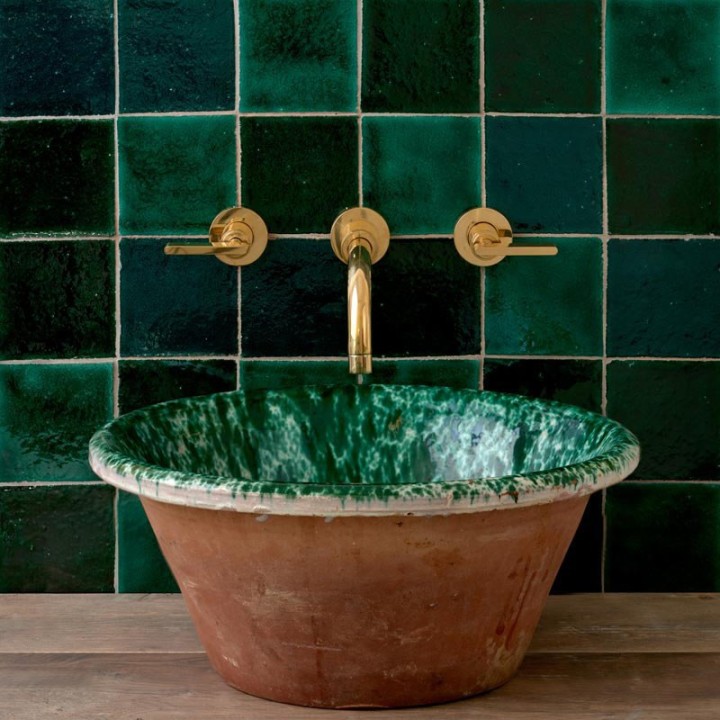Compilation of different shades of green square tiles behind an antique ceramic bowl with green marble tones and gold taps