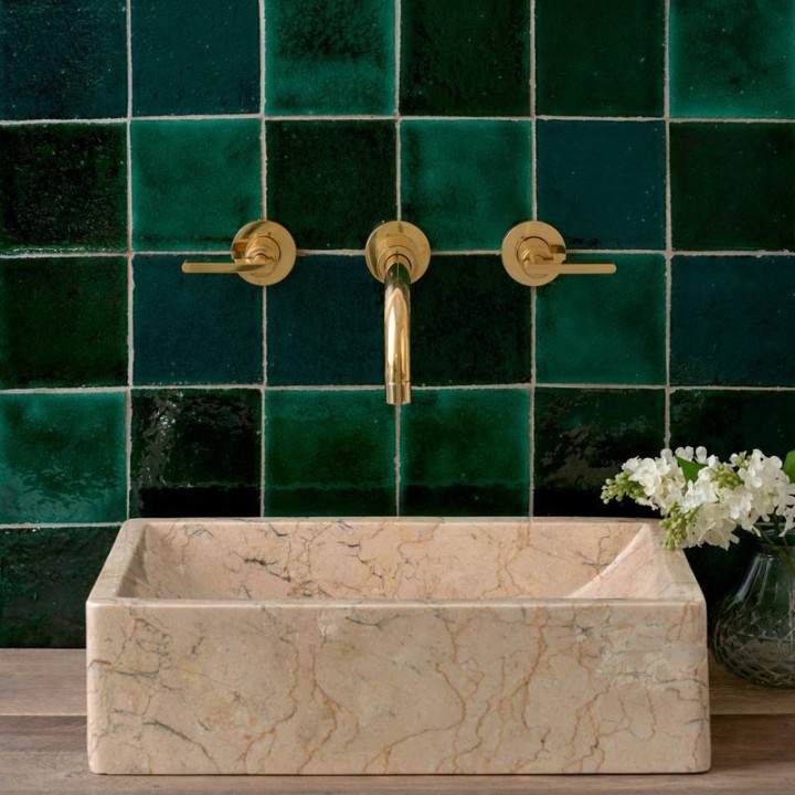 Compilation of different shades of green square tiles behind a rectangle sandstone basin and gold taps