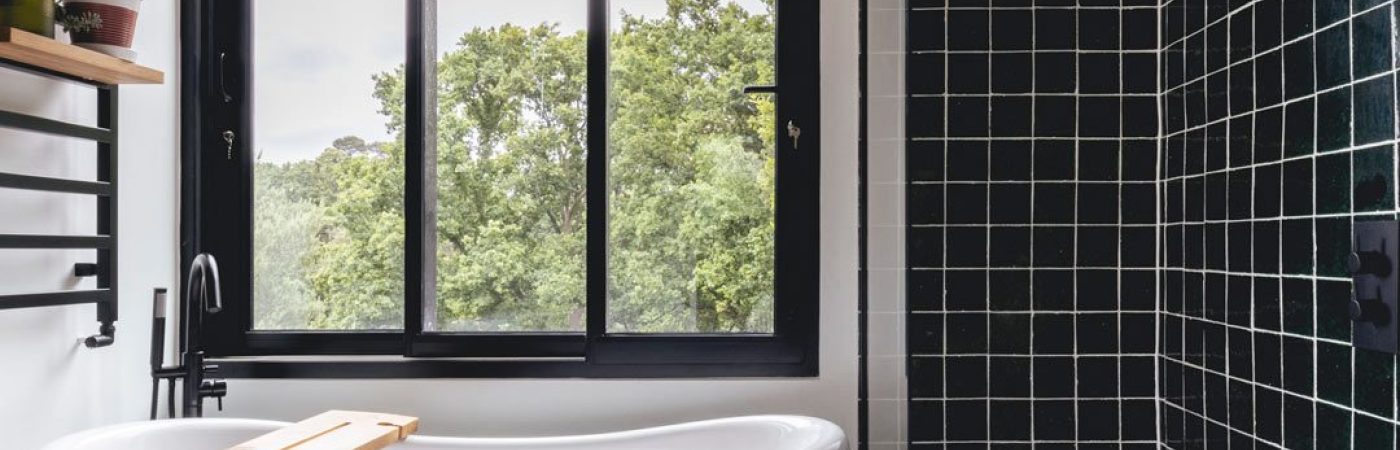 Minimalist bathroom with a walk in shower featuring bottle green square tiles next to a freestanding green roll top bath