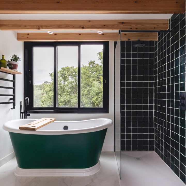 Minimalist bathroom with a walk in shower featuring bottle green square tiles next to a freestanding green roll top bath