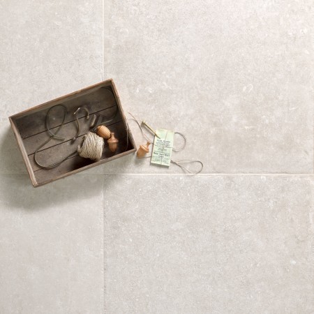 Creamy stone effect square porcelain floor tile with beige grout and a box of assorted items
