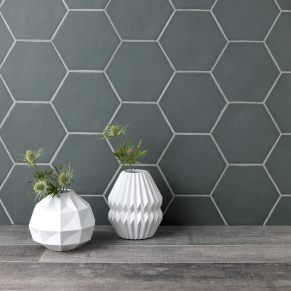 Wall of cool grey matt hexagon tiles behind a grey oak work top and  styled with white vases