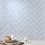 Wall of skinny pale blue matt metro tiles with silver grey grout laid in a herringbone tile pattern styled with a pile of plates