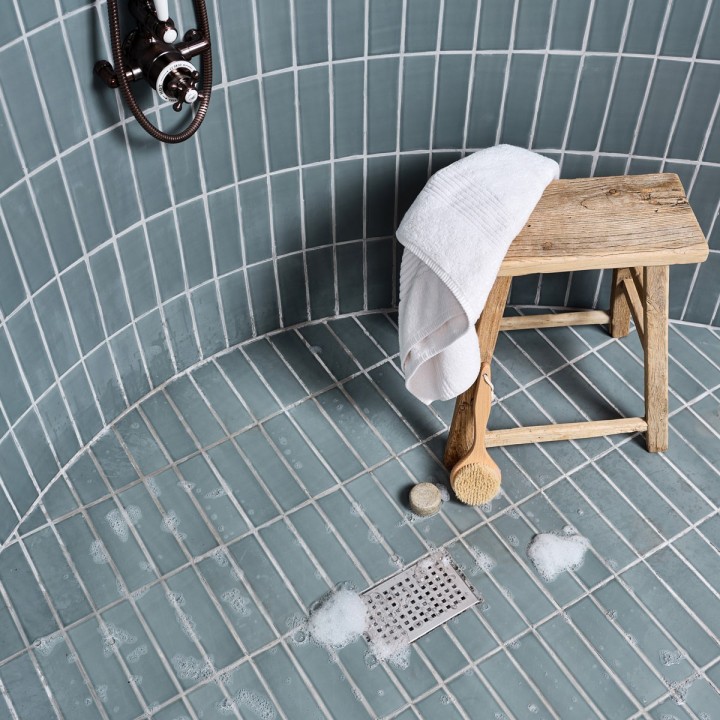 Shower tray tiled in a teal green skinny metro matt tile with a chrome drain and milking stool to the side