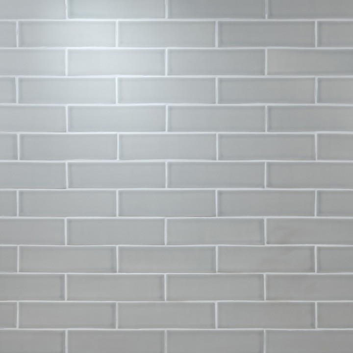 Wall of skinny pale green matt metro tiles with silver grey grout laid in a brick bond tile pattern