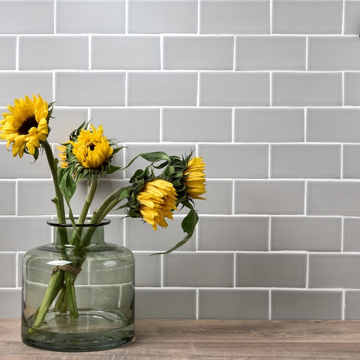 Wall of pale green matt metro tiles with white grout styled with a green vase and sunflowers