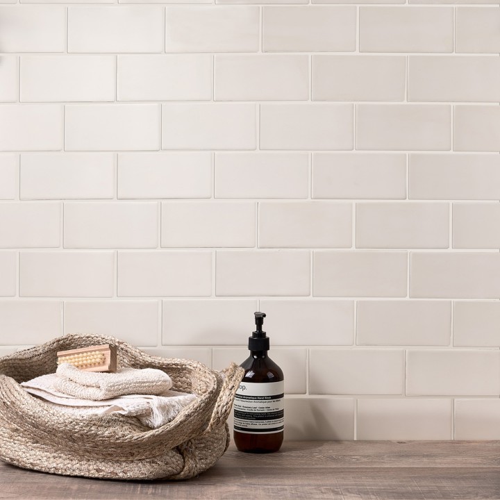 Wall of neutral warm white matt metro tiles with jasmine grout styled with bathroom accessories and toiletries