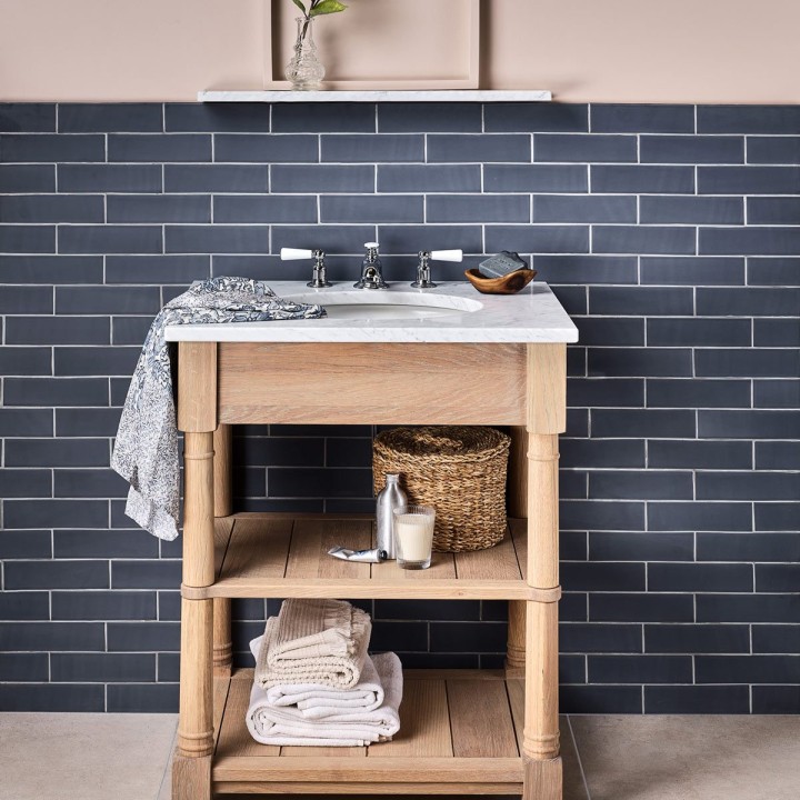Wall of slate blue skinny metro tiles behind a vanity unit paired with a sandstone porcelain floor