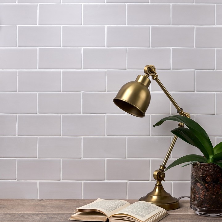 Wall of stone grey matt metro tiles with white grout styled with a lamp and book