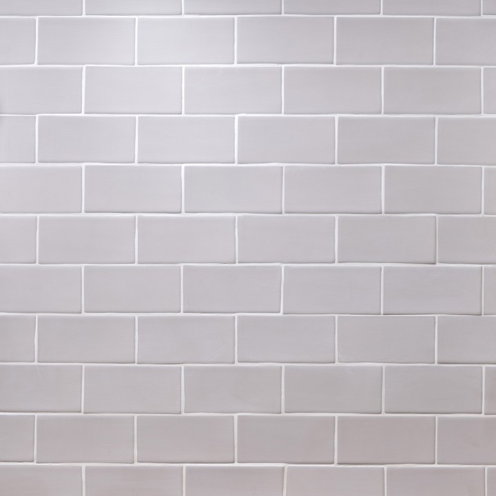 Wall of stone grey matt tiles with silver grey grout laid in a brick bond tile pattern