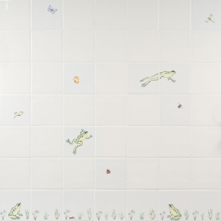 Wall of ivory tiles with hand painted sitting and leaping frogs, pond grasses and insects