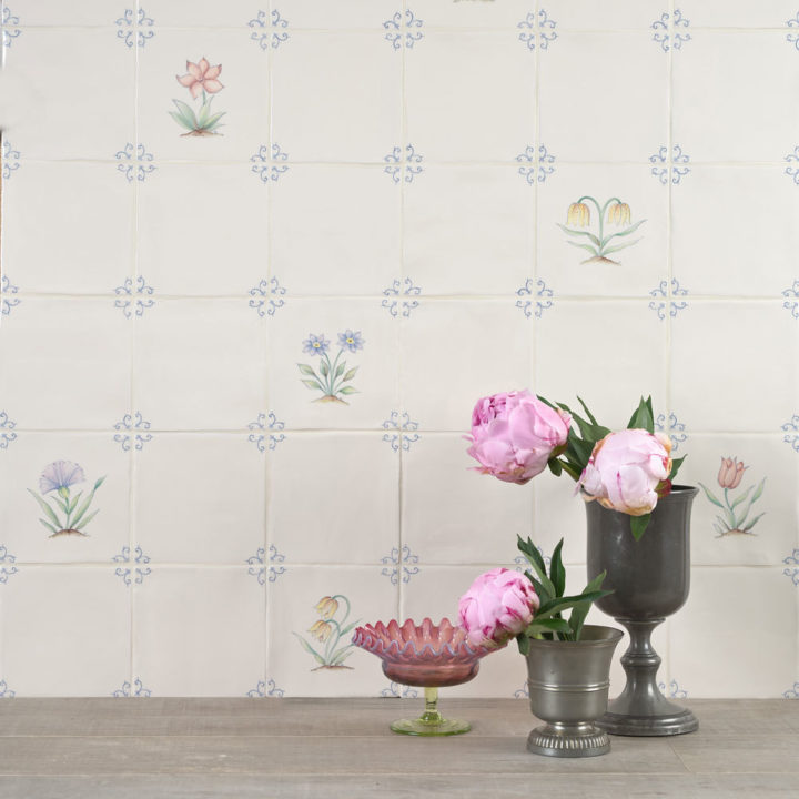 Wall of polychrome delft flower tiles paired with plain tiles behind an oak work top and some flowers