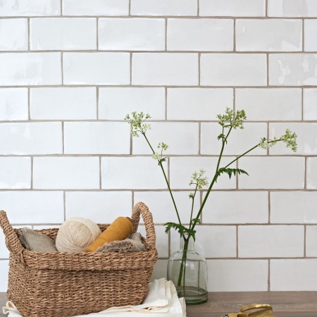 Wall of soft white metro brick tiles behind an an oak worktop and a basket of bread
