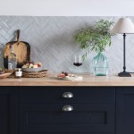 Wall of grey brick tiles laid in herringbone pattern behind navy kitchen cabinets