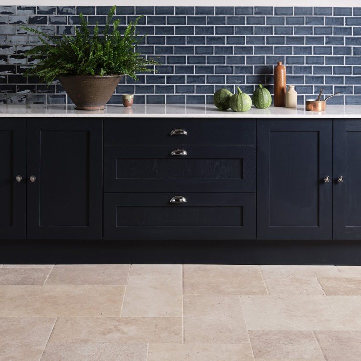 Navy metro brick tiles finished with white grout behind navy kitchen cabinets with kitchen accessories on top and a french limestone floor.