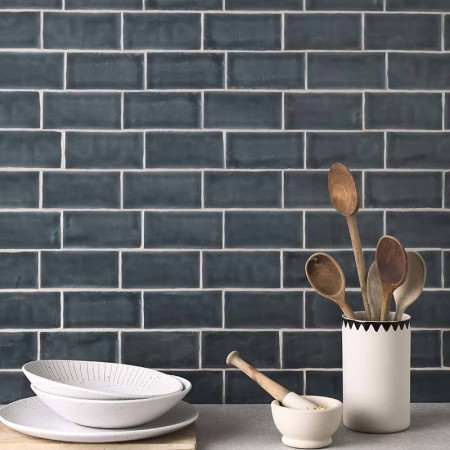Wall of metro dark grey handmade wall tiles behind a marble work top and kitchenware