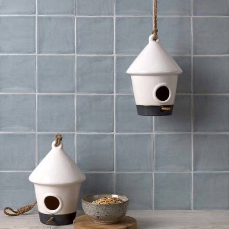 Wall of square medium grey handmade wall tiles behind a grey wood work top and bird feeders