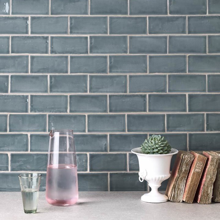 Wall of metro grey blue handmade wall tiles behind a marble worktop and home accessories