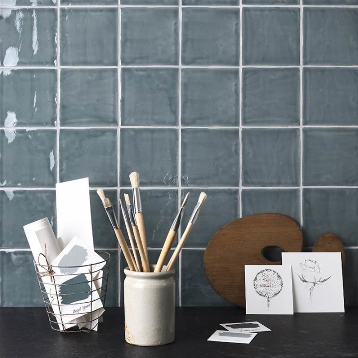 Wall of square grey blue handmade wall tiles behind a slate top and artist accessories