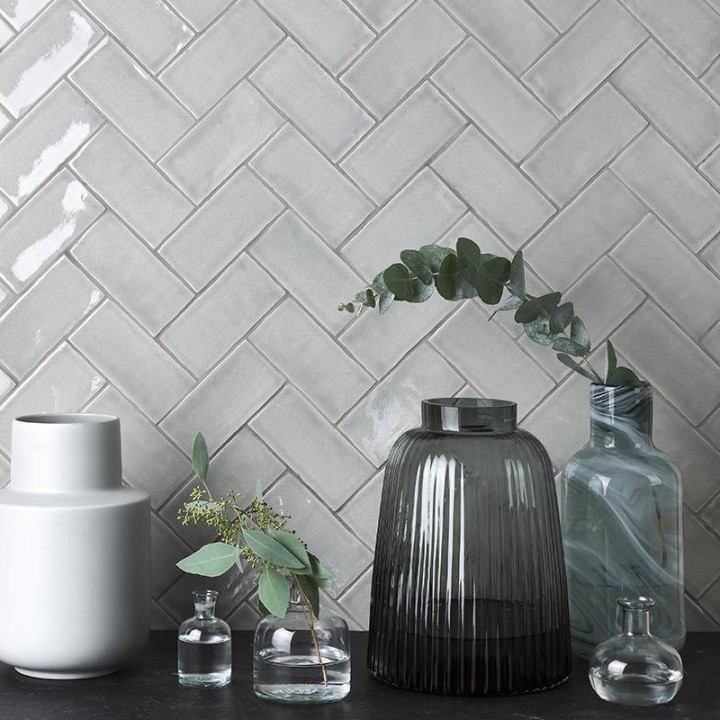 Wall of metro grey handmade wall tiles behind glass vase laid in a herringbone tile pattern