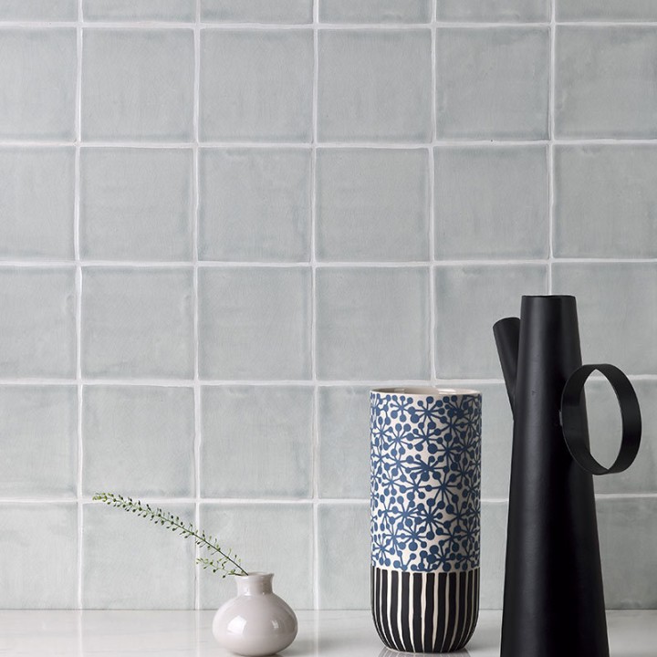 Wall of square grey handmade wall tiles behind a marble work top and modern vases