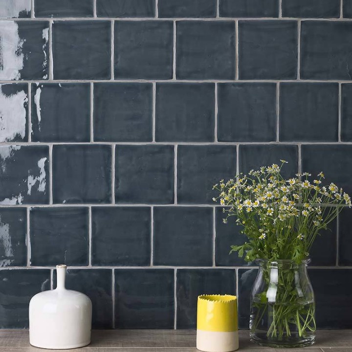 Wall of square dark navy blue handmade wall tiles behind a grey wood work top and vases