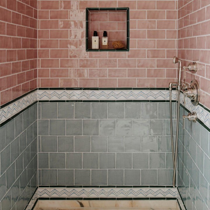 Light grey-blue wall tiles used in a shower area with a handpainted tile border and pink wall tiles above