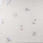 Wall of antique white square tiles with seaside illustrations like deck chairs, beach huts and boats.