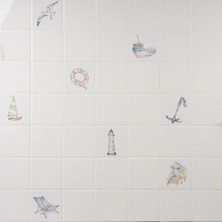 Wall of antique white square tiles with seaside illustrations like deck chairs, beach huts and boats.