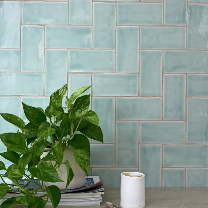 Wall of gloss cool blue medium metro tile laid in a vertical herringbone tile pattern behind a pothos