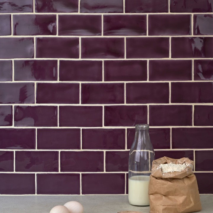 Wall of gloss plum purple medium metro tile laid in a brick bond tile pattern behind kitchen accessories