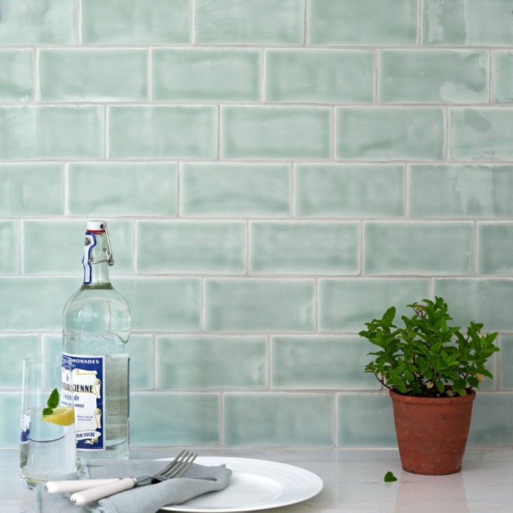 Wall of gloss cool blue green medium metro tile laid in a brick bond tile pattern behind a dining accessories