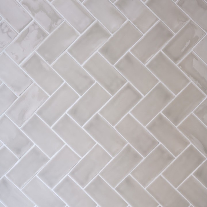 Wall of gloss warm grey medium metro tile laid in a vertical herringbone tile pattern finished with white grout