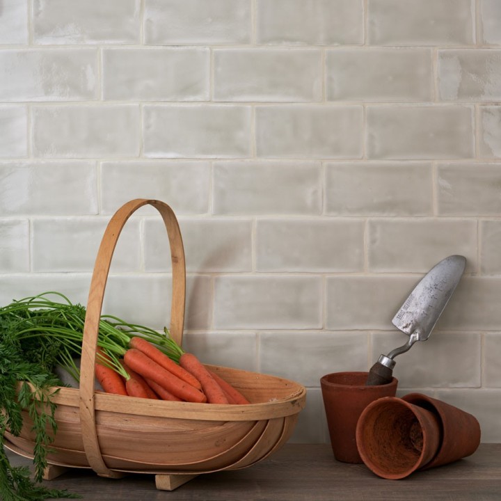 Wall of gloss neutral green medium metro tile laid in a brick bond tile pattern behind gardening accessories