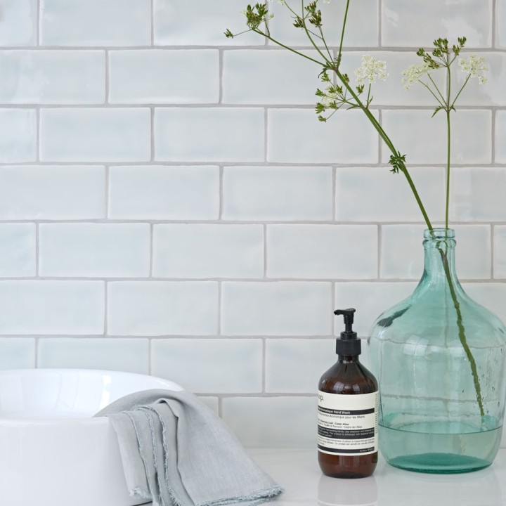 Wall of gloss neutral cool white medium metro tile laid in a brick bond tile pattern behind bathroom accessories